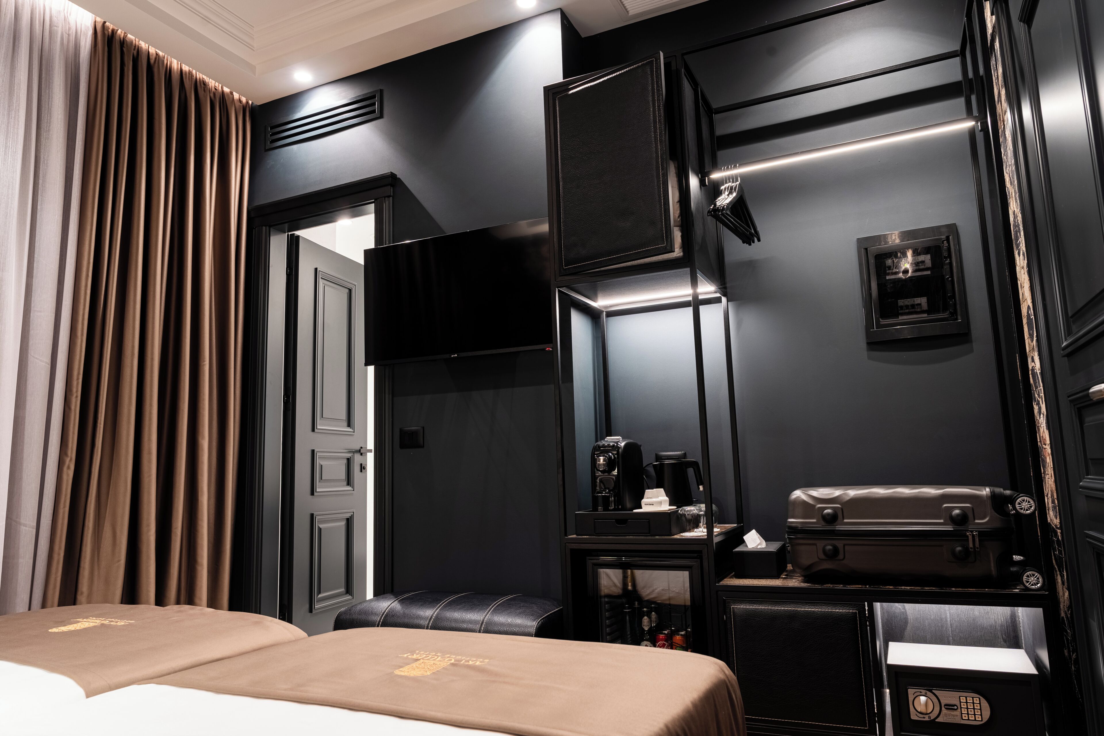 Camera d'albergo con un letto, una scrivania con una macchina del caffè, una valigia e un televisore.