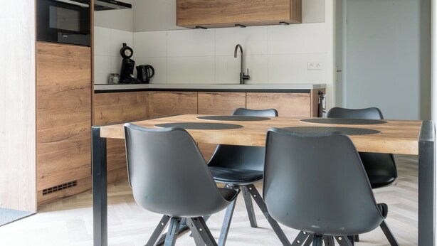 Une cuisine moderne avec une table en bois et des chaises noires, un four encastré et un luminaire suspendu.