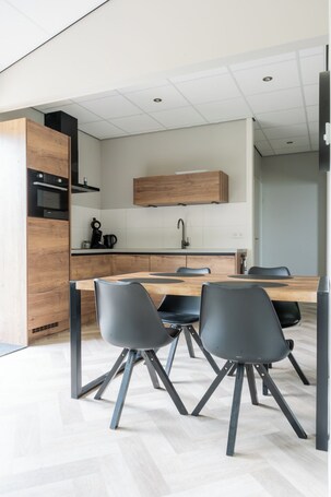 A modern kitchen with a wooden table and black chairs, a built-in oven, and a hanging light fixture.