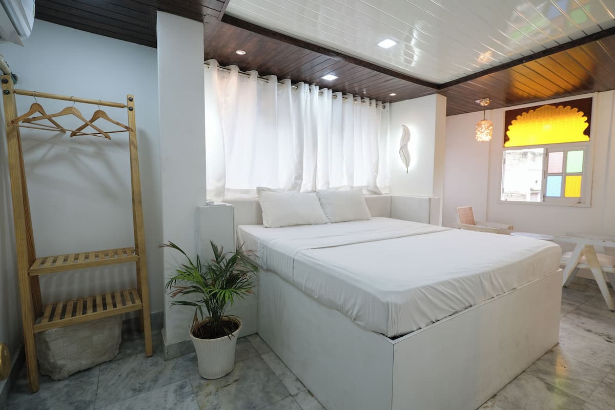 A bedroom with a large bed, a wooden shelf, a potted plant, and a window with curtains.