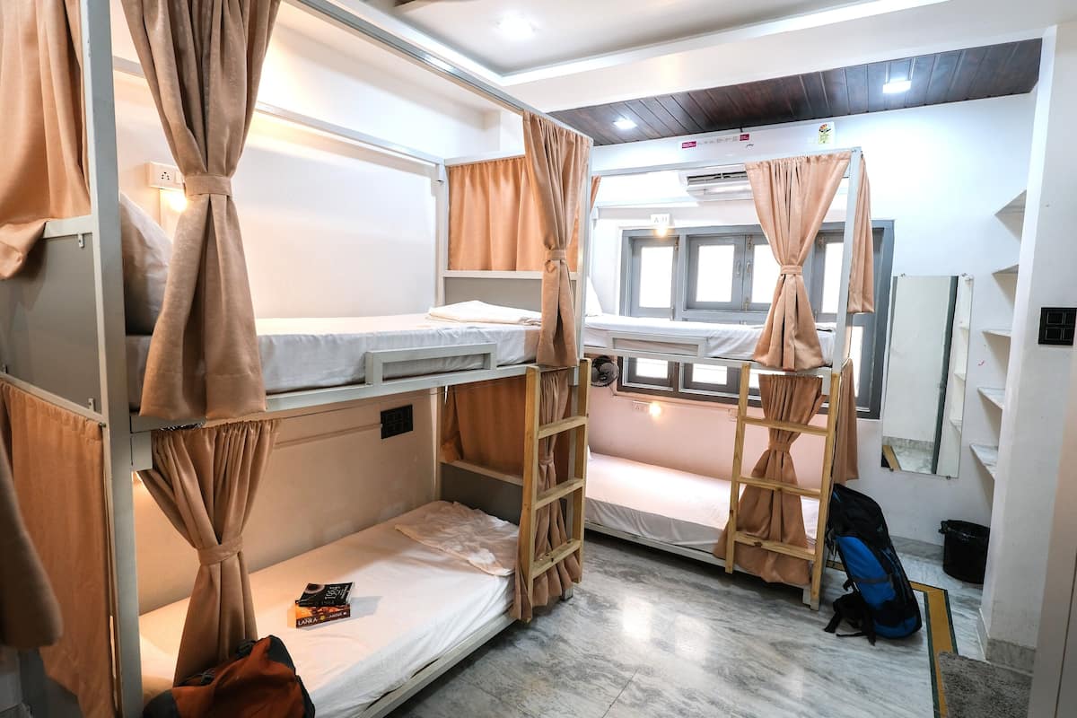 A bunk room with two beds, curtains, a ladder, a backpack, and a window.