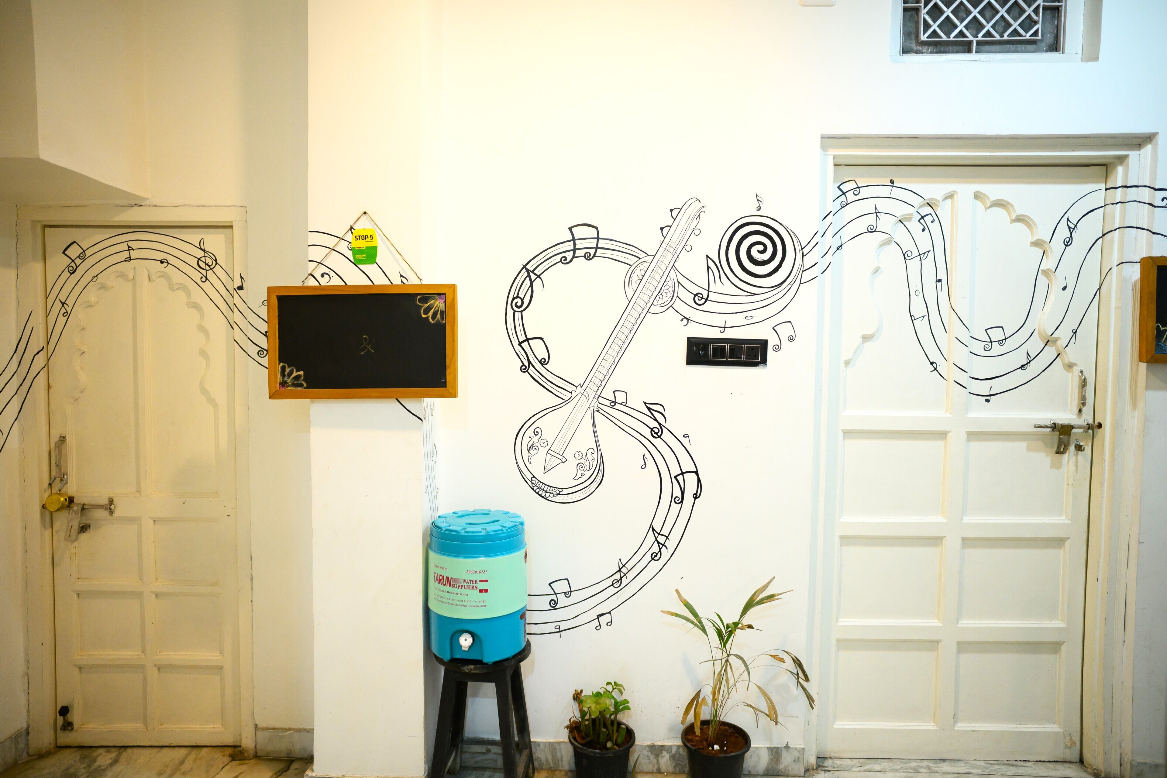 Un pasillo con un mural, un dispensador de agua y dos plantas en macetas.