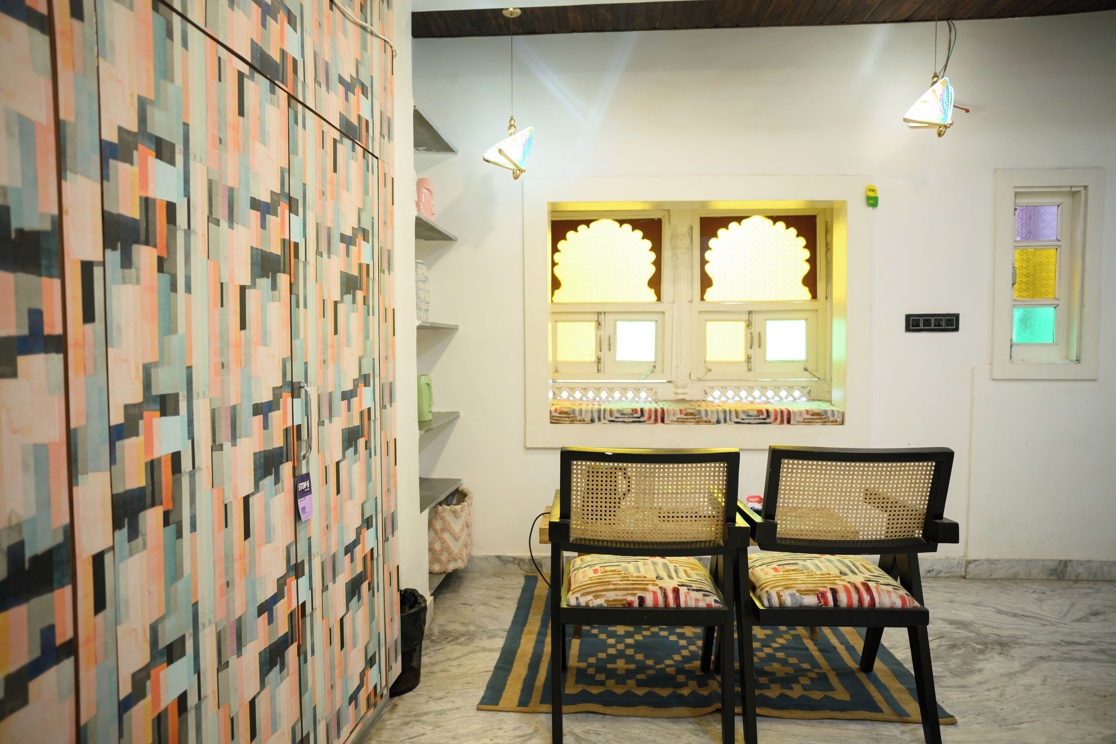 A room with a patterned wall, two wicker chairs, a window with decorative glass, and hanging lights.