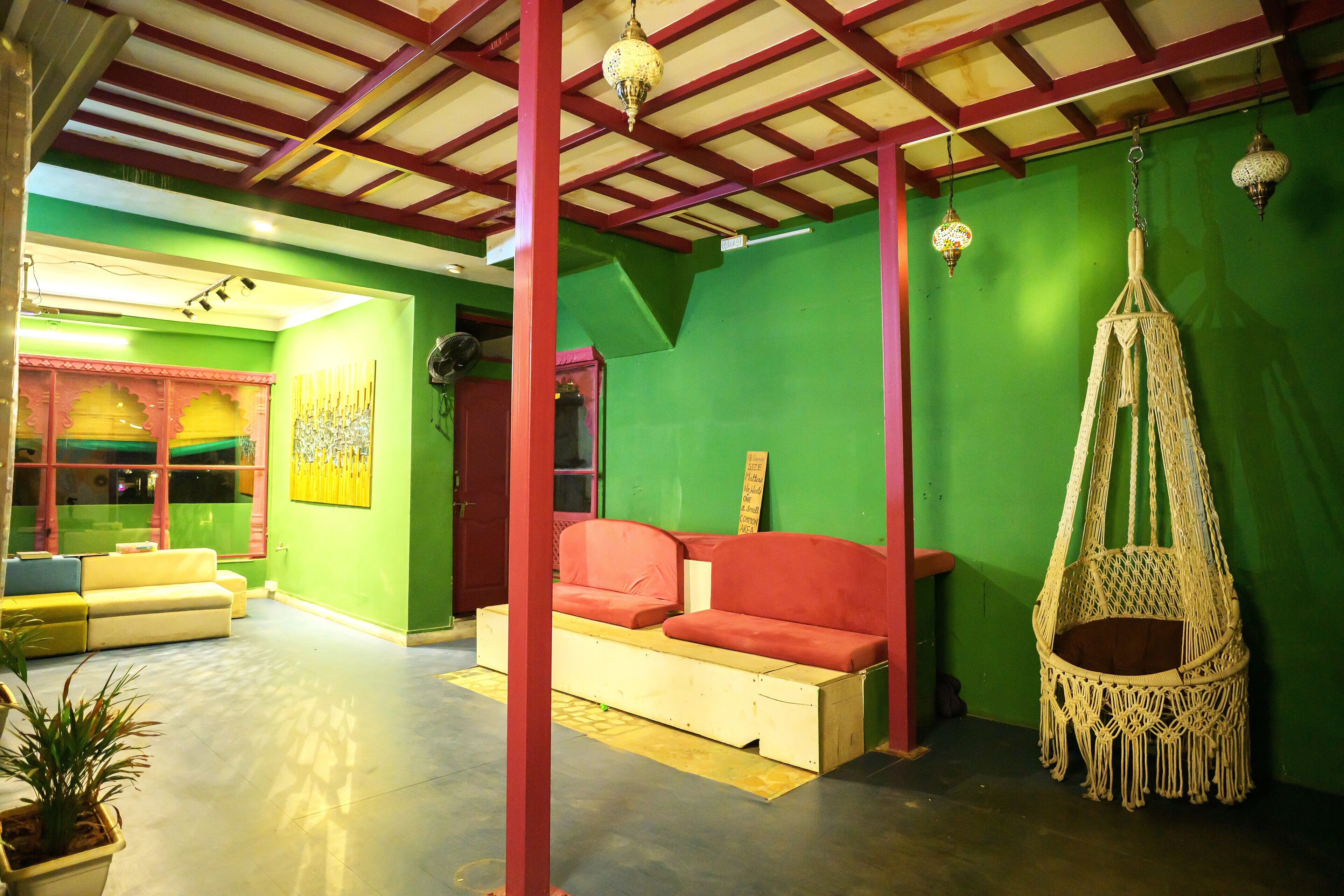 A room with a green wall, a red sofa, a hanging macrame chair, and a wooden bench.