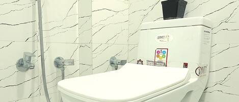 A white toilet with a marble-patterned wall and a shower head to the left.