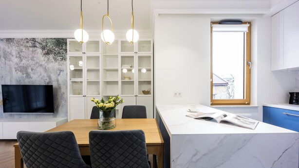 A modern kitchen with white cabinets, a marble island, and pendant lighting. - Native Apartments Orawska 14 (Kraków)