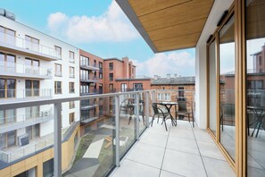 Un immeuble d’appartements moderne doté d’un balcon avec des garde-corps en verre, un plafond en bois et un espace salon extérieur.