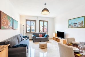 Een moderne woonkamer met een bank, een televisie en een eethoek met een tafel en stoelen.