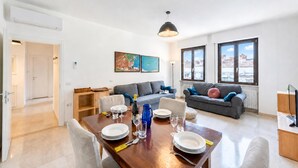A modern living room with a dining area, grey sofas, a coffee table, and large windows with a view. - Casa Lucia in Old Riva Town With Balcony View (Riva del Garda)