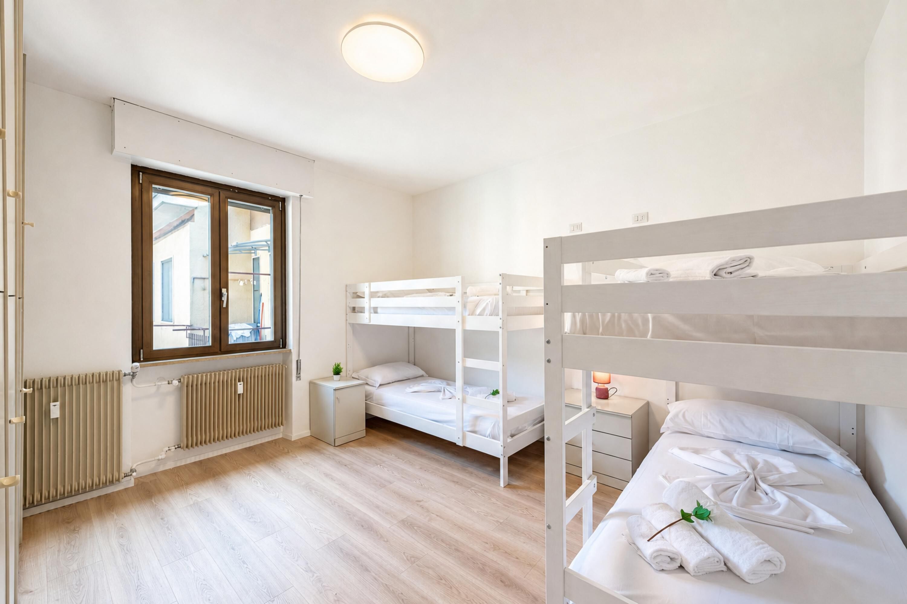 A room with bunk beds, a window, a radiator, and a bedside table with a lamp.