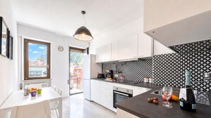 A modern kitchen with white cabinets, a black and white patterned backsplash, and a dining area with a table and chairs. - Casa Lucia in Old Riva Town With Balcony View (Riva del Garda)