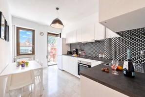 A modern kitchen with white cabinets, a black and white patterned backsplash, and a dining area with a table and chairs. - Casa Lucia in Old Riva Town With Balcony View (Riva del Garda)