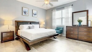 Une chambre d’hôtel moderne avec un grand lit, un ventilateur de plafond, une table de chevet avec une lampe, une commode et une fenêtre avec des rideaux.