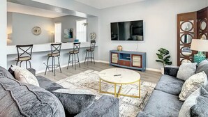 Un salon moderne avec un canapé, une table basse et des fauteuils. Un téléviseur est fixé au mur et un ventilateur de plafond est installé.