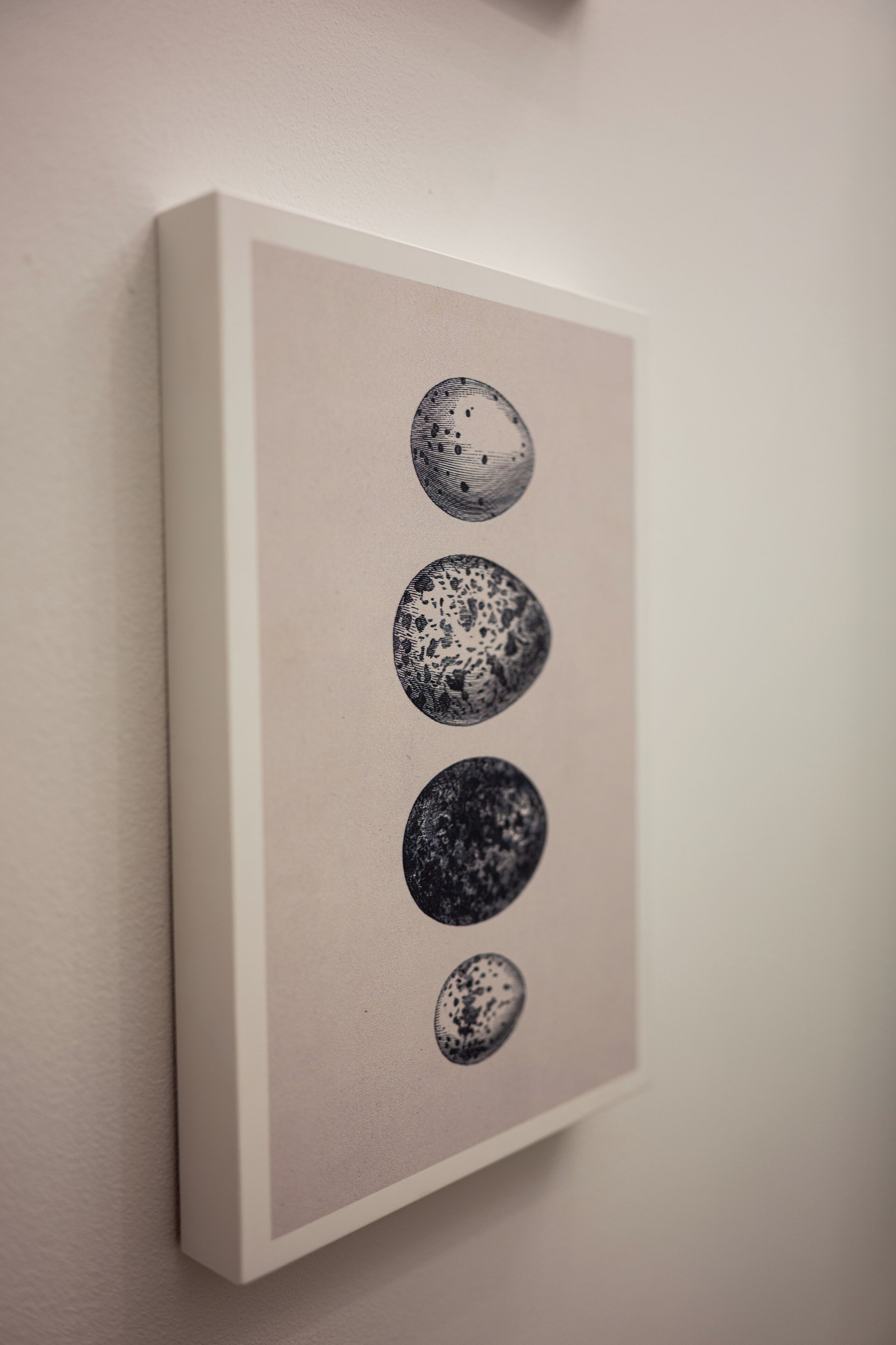 A framed artwork with four circular designs on a white wall.