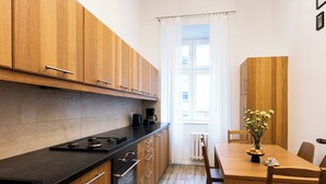 A modern kitchen with wooden cabinets, a black countertop, and a dining area with a wooden table and chairs. - Native Apartments Skawińska 5 (Kraków)