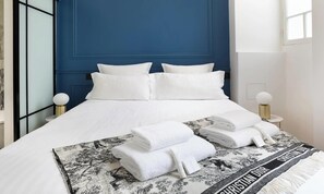 Ett hotellrum med en stor säng, vita sängkläder och en blå accentvägg. Det finns två sängbord med lampor och ett fönster med utsikt.