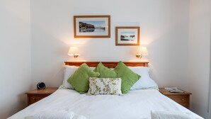 A neatly made bed with white linens, green and patterned pillows, and two framed pictures on the wall above. - Minffordd Cottage, Moelfre - sleeps 4 guests  in 2 bedrooms (Moelfre)