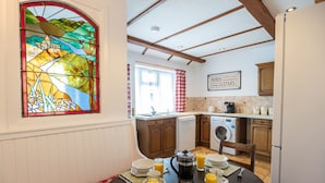 A cozy kitchen with wooden cabinets, a dining table set for breakfast, and a stained glass window. - Minffordd Cottage, Moelfre - sleeps 4 guests  in 2 bedrooms (Moelfre)