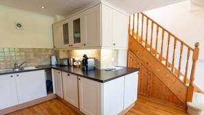 Une cuisine avec des meubles blancs, un escalier en bois et un pare-feu en carreaux.
