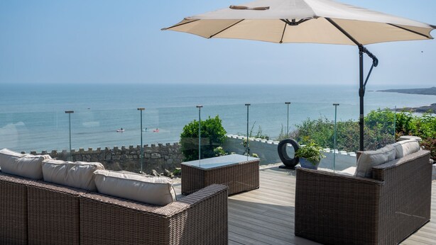 Um deck com mobiliário de vime e um grande guarda-sol, com vista para o mar.