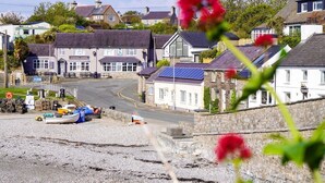 Un poble costaner amb edificis de pedra tradicionals, un bar anomenat 'KINMEL ARMS' i una platja de grava amb vaixells.