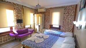 Une pièce avec un mur en briques, un lit avec une literie à motifs, un canapé violet et un téléviseur fixé au mur.