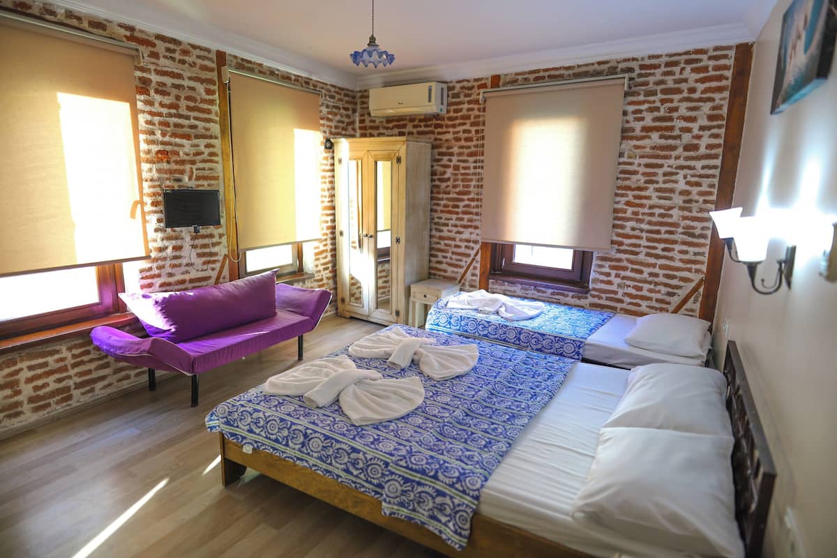 A room with a brick wall, a bed with patterned bedding, a purple sofa, and a TV on the wall.