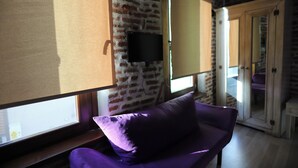 Une pièce avec un mur en briques, un téléviseur fixé au mur, un fauteuil violet et un meuble en bois.