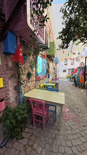 A cobblestone street with colorful outdoor seating and a building with a balcony. - Rengarenk Pansiyon (Ayvalik)