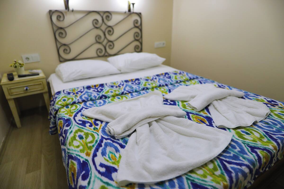 A neatly made bed with a patterned bedspread and two white towels folded on top.