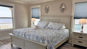 A bedroom with a bed, two nightstands, a ceiling fan, and a view of the ocean.