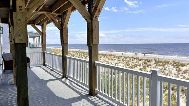 A wooden deck with a white railing overlooking a beach.