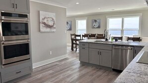 A modern kitchen with built-in ovens, a large island with a sink, and a view of the ocean through large windows.