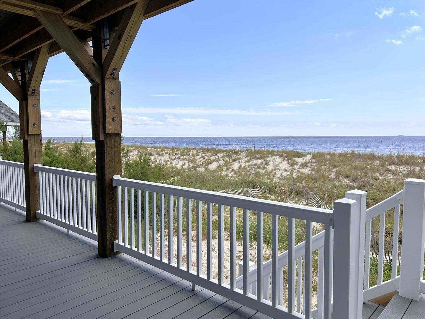 Une terrasse en bois, agrémentée de rampes blanches, qui offre une vue sur une plage bordée de dunes de sable et sur l’océan.
