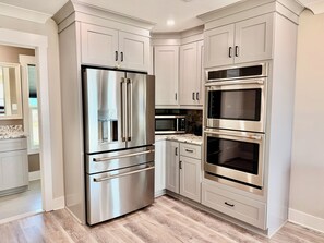 Une cuisine moderne dotée d’appareils électroménagers en acier inoxydable, de meubles blancs et d’un plancher en bois.