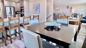 Une cuisine moderne équipée d’appareils électroménagers en acier inoxydable, un coin repas avec des chaises en bois et une table sombre, et un salon avec un canapé et des œuvres d’art décoratives au mur.