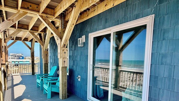 Une terrasse en bois offrant une vue sur l’océan, une grande porte-fenêtre coulissante et une petite table en bois.