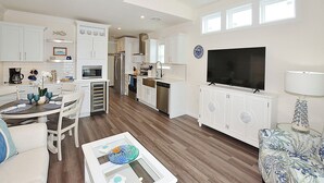 A modern kitchen with white cabinetry, a large flat-screen TV, and a dining area with a round table and chairs.