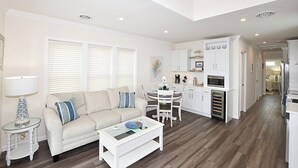A compact living space with a sofa, coffee table, dining area, kitchenette, and a hallway leading to a bedroom.