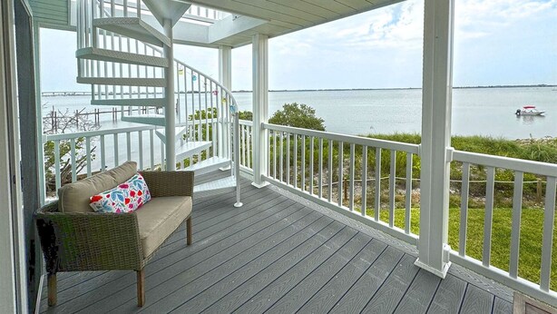 A covered porch with a spiral staircase, a wicker chair with a cushion, and a view of a body of water with a boat.