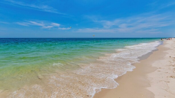 Une plage avec une eau turquoise et limpide, un rivage sablonneux et quelques personnes au loin.