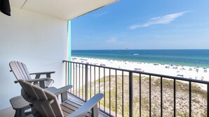 Un balcon avec deux fauteuils Adirondack, une vue sur une plage parsemée de parasols et un ciel bleu dégagé.