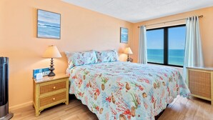 Une chambre à coucher comprenant un lit, deux tables de chevet, un téléviseur fixé au mur et une fenêtre donnant sur la mer.