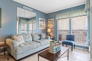 Uma sala de estar com um sofá azul claro, uma poltrona azul, uma mesa de centro de madeira e uma mesinha de cabeceira com uma luminária.