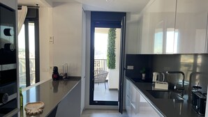 Eine moderne Küche mit schwarzem Arbeitsplatz, Edelstahlgeräten und Blick auf einen Balkon mit einem Blumentopf.