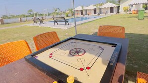 A table with a tabletop game, outdoor seating, and a view of a swimming pool and buildings in the background.