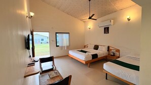 A hotel room with two beds, a desk, a chair, a TV, and a ceiling fan.