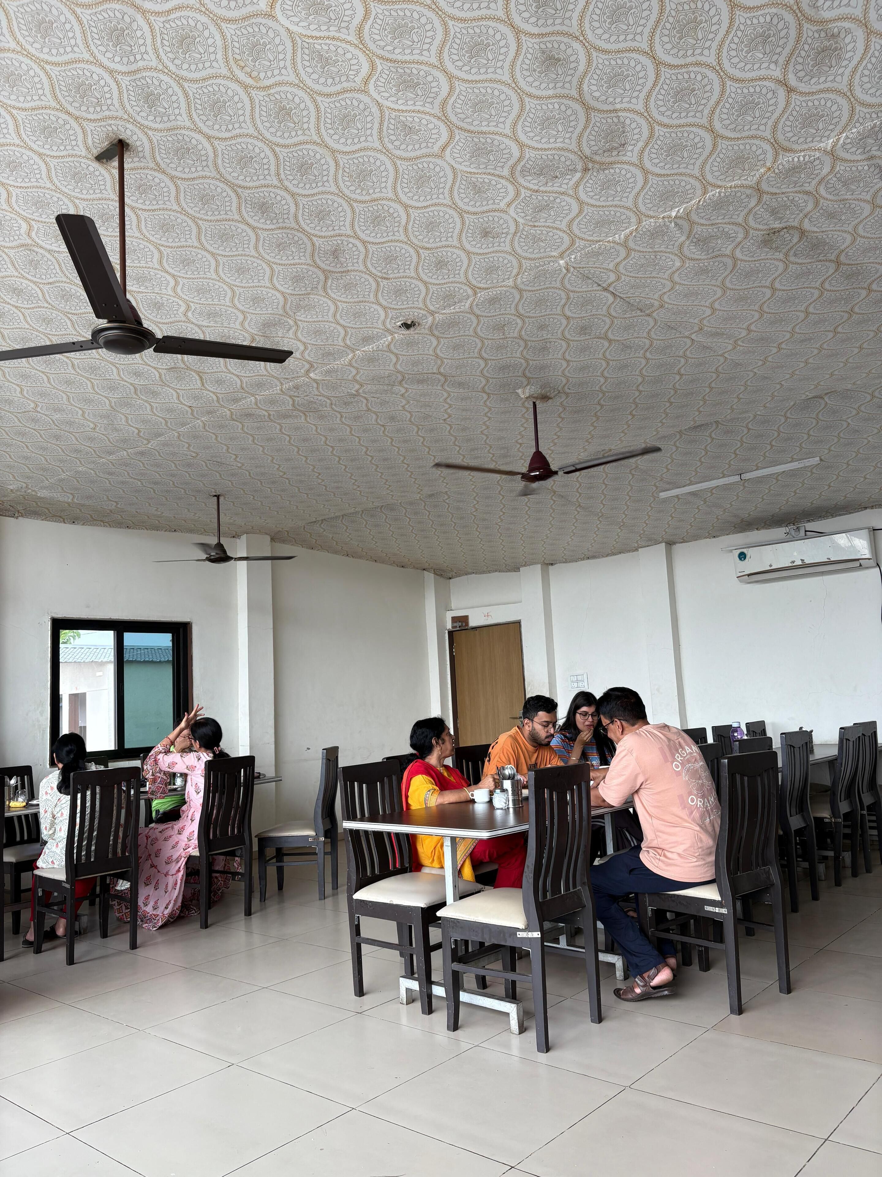 A dining area with multiple tables and chairs, ceiling fans, and an air conditioning unit.