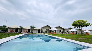 Una piscina con edificios cercanos, asientos exteriores y una zona verde.